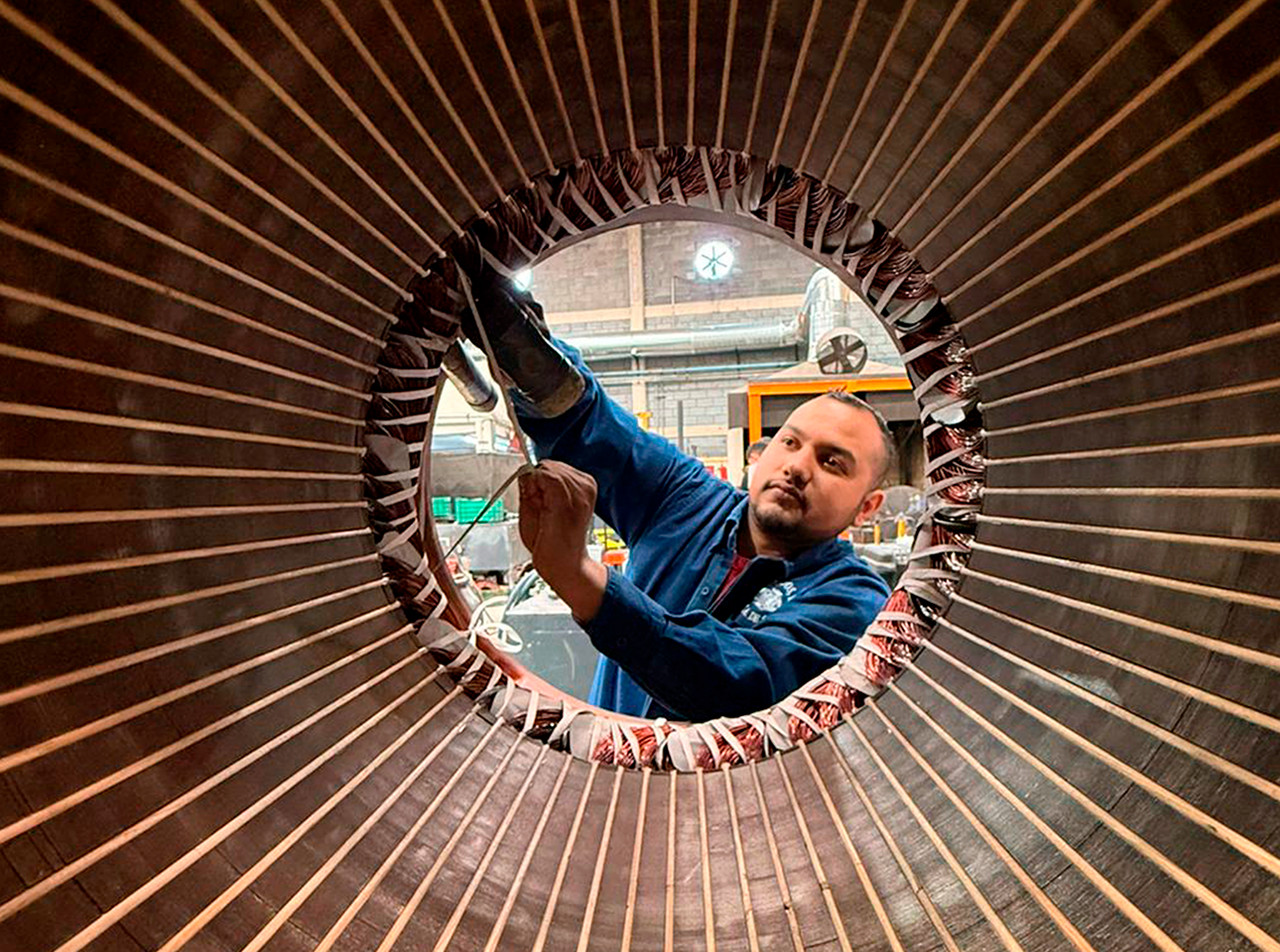 Técnico realizando el bobinado de estator en motor eléctrico industrial durante proceso de rebobinado.