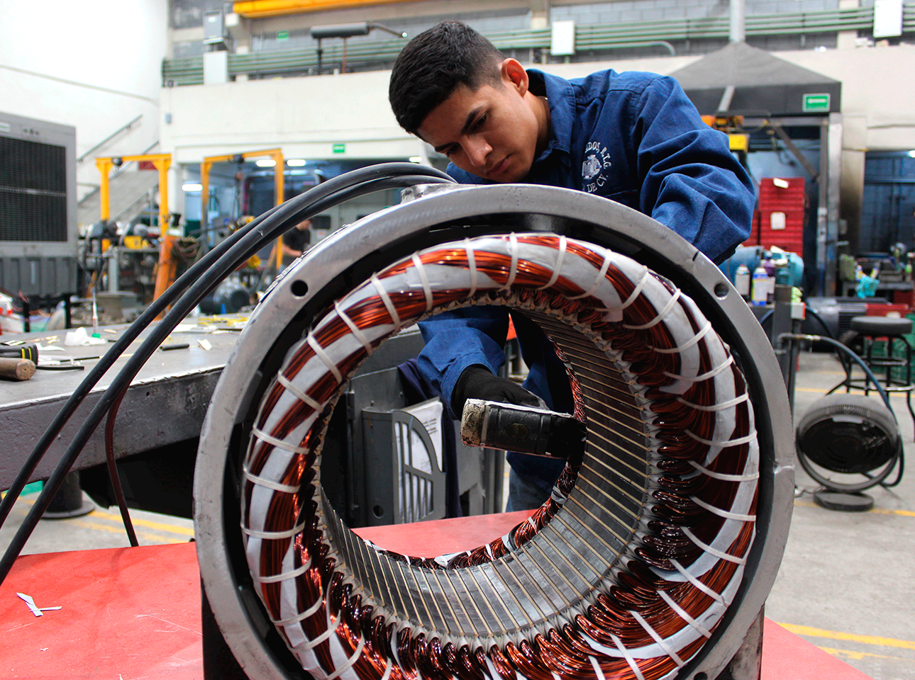 Técnico realizando el proceso de embobinado con alambre de cobre en el estator de un motor eléctrico industrial.