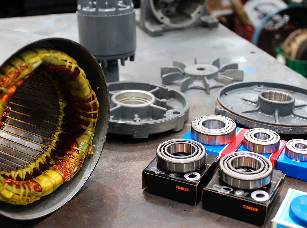 Componentes de motor eléctrico desarmado sobre mesa de trabajo: estator, baleros nuevos, tapas y ventiladores.