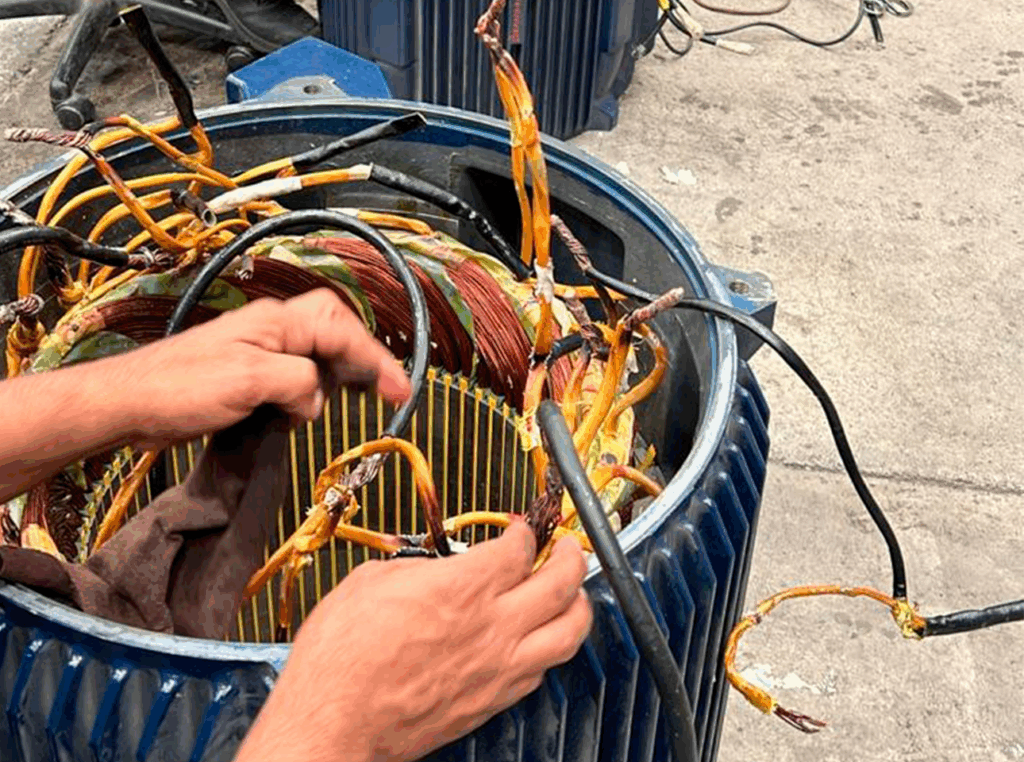 Técnico conectando cables de motor eléctrico industrial durante proceso de mantenimiento electromecánico.
