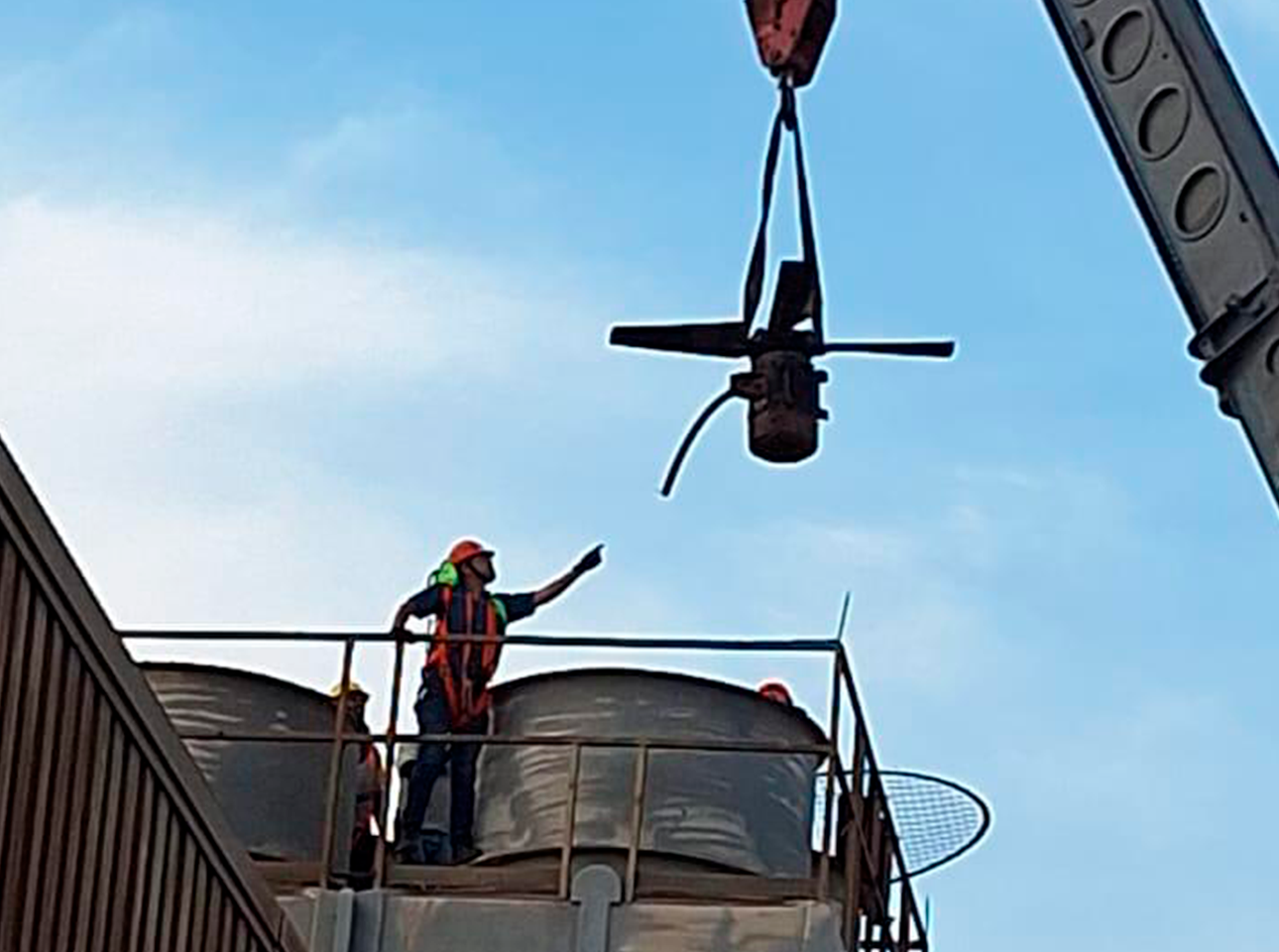 Técnicos industriales guiando el desmontaje de un ventilador axial mediante grúa en planta.